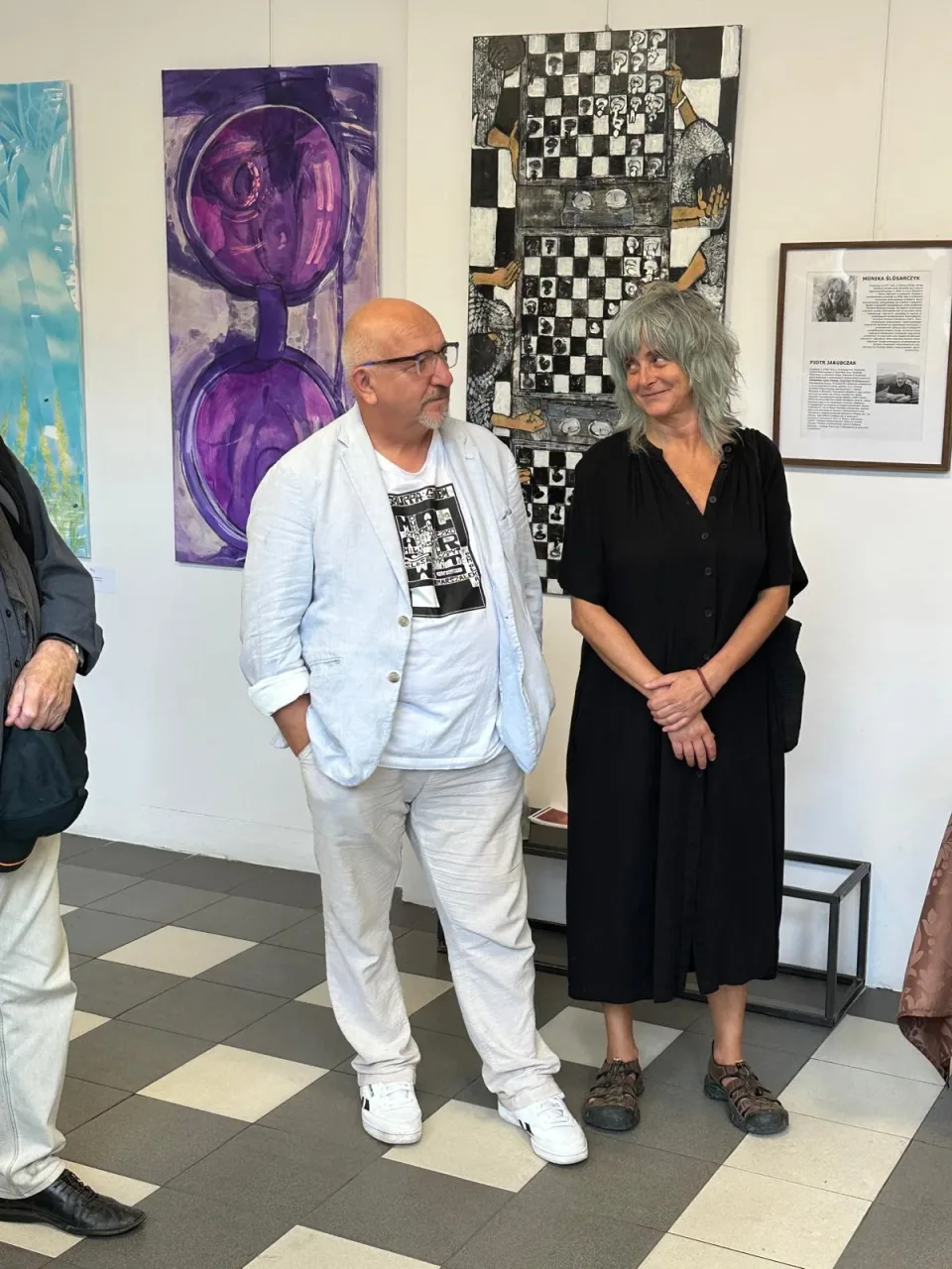 Guests at the opening of Między piekłem a niebem at Arteon in Warsaw, photographed in front of the exhibited paintings.