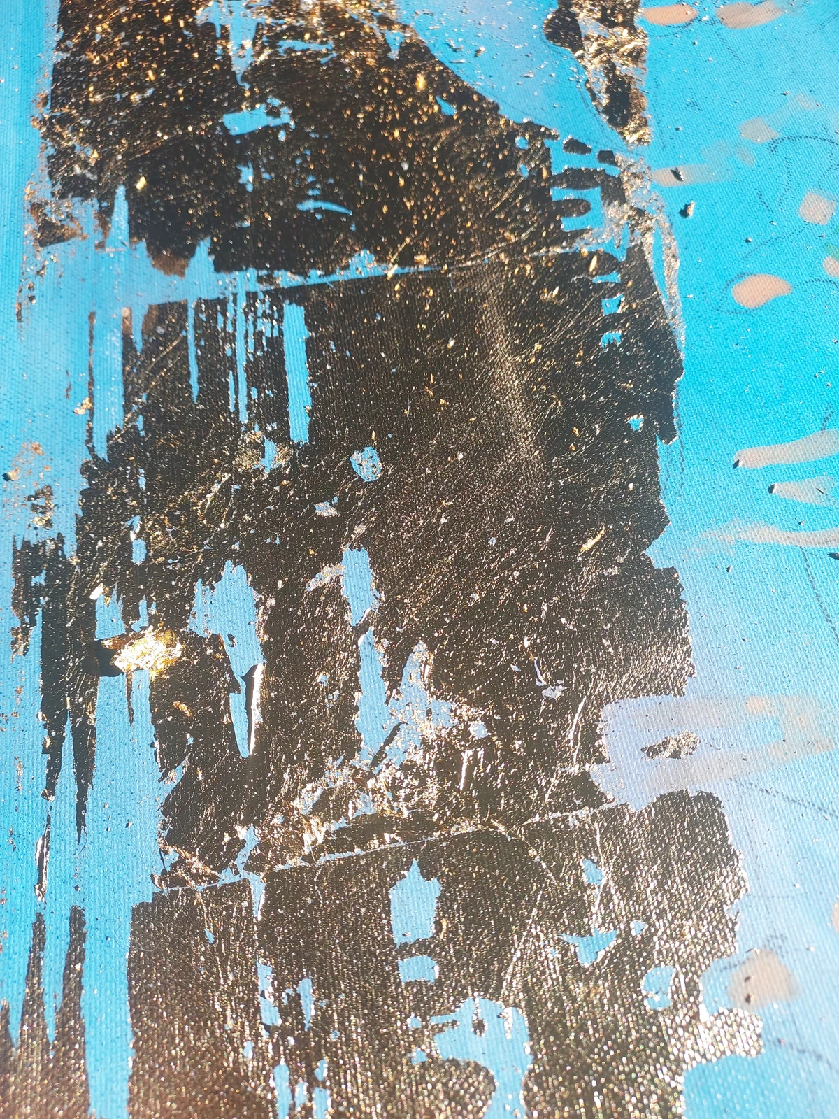 Close view of dark and gilded layers across a blue painted canvas.